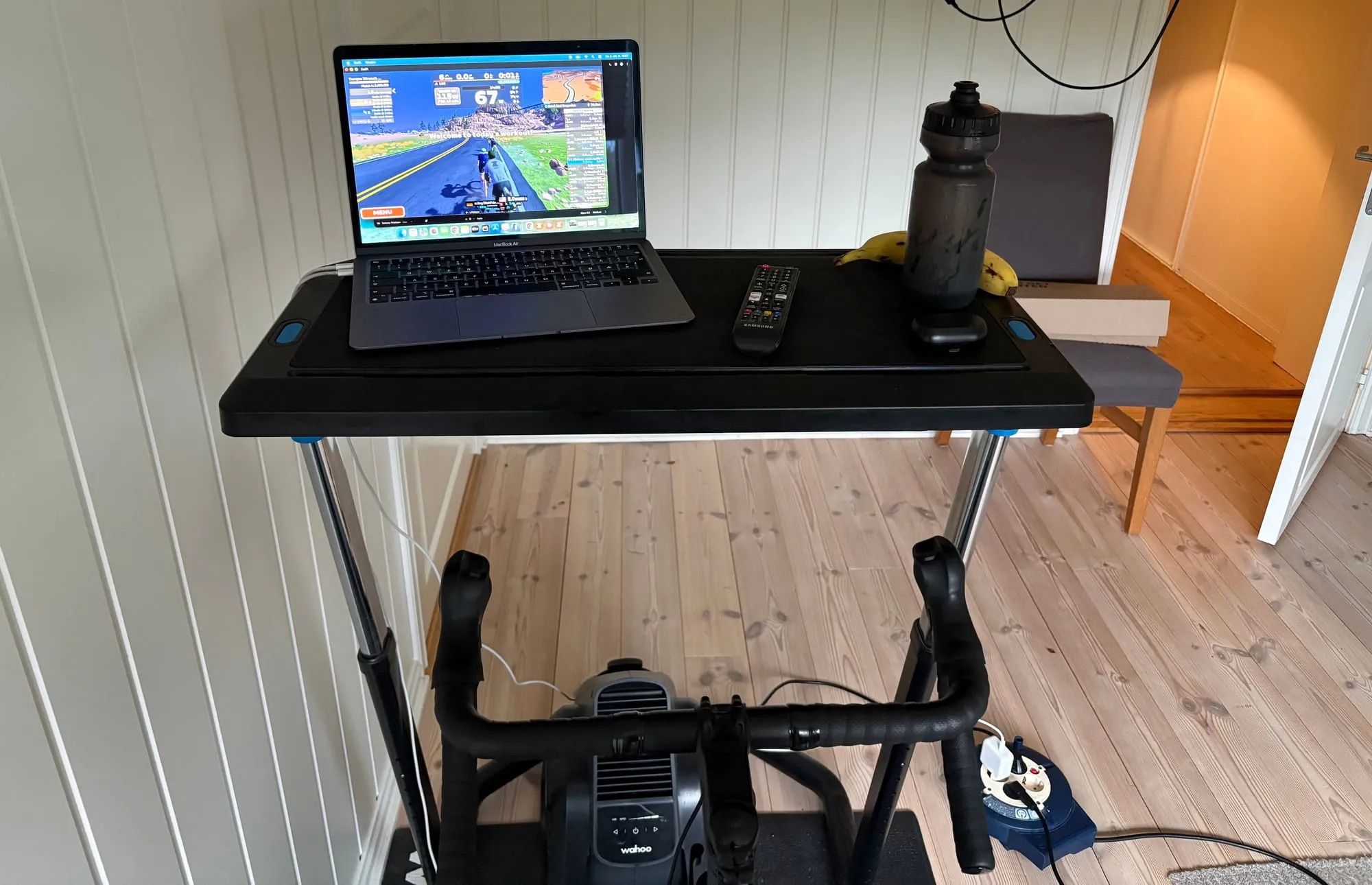 Bærbar Mac med Zwift på skjermen, på et rullebord foran styret på en smart bike